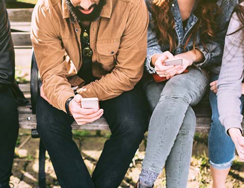 Row of friends sitting on bench with phones.