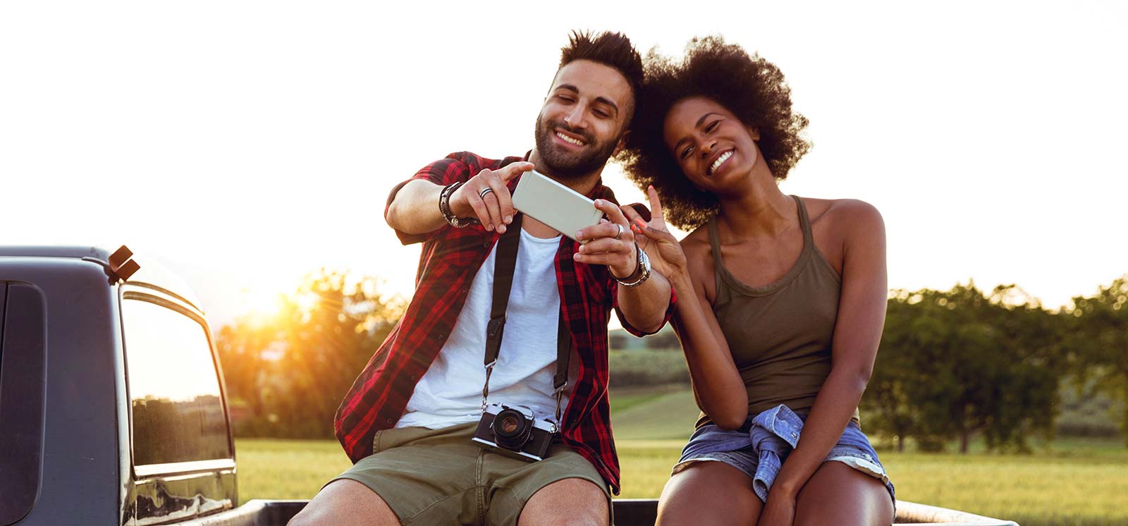 Young couple sitting on pick up truck taking selfie.