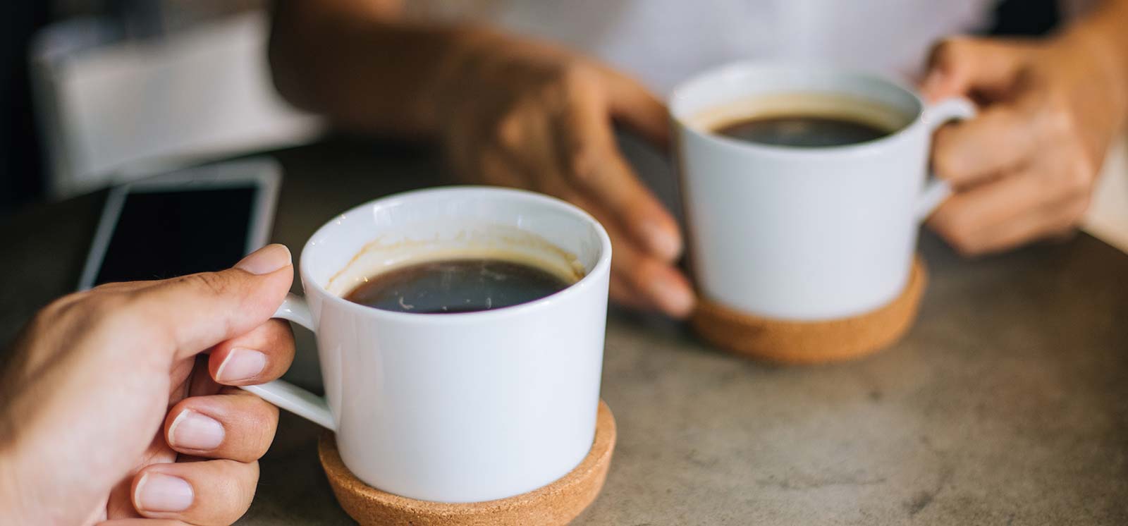 Two woman having coffee, with phone on table.