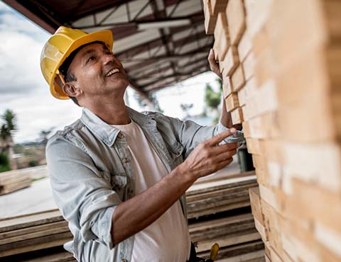 Man wearing construction hat looking at pile of 2x4's.